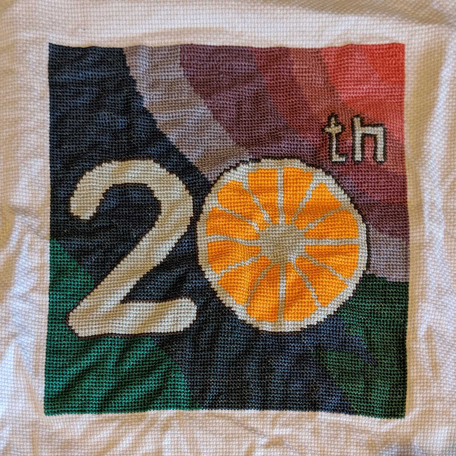 Cross-stitch reading '20th' with orange slice