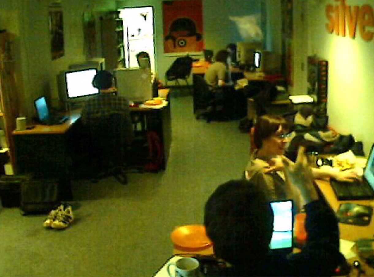 Dark webcam image of people playing PC games in an office