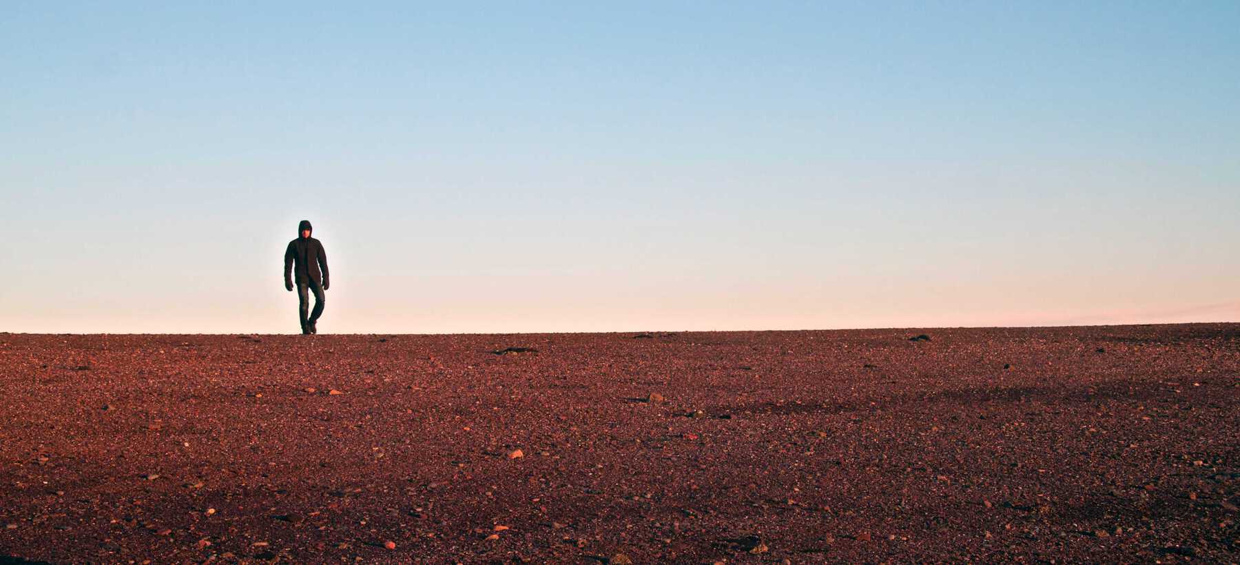Person in winter coat walking on barren reddish sand